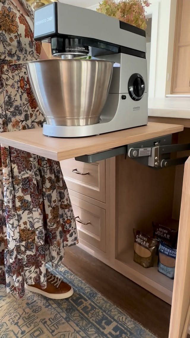 A silver stand mixer sits on a wooden shelf extended by a mechanical appliance lift mechanism.