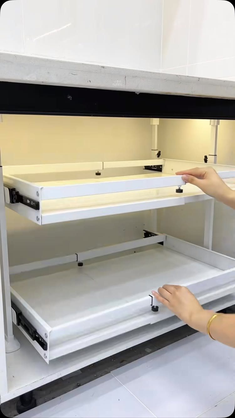 Hands pulling out two white rectangular drawers from a white kitchen storage unit.