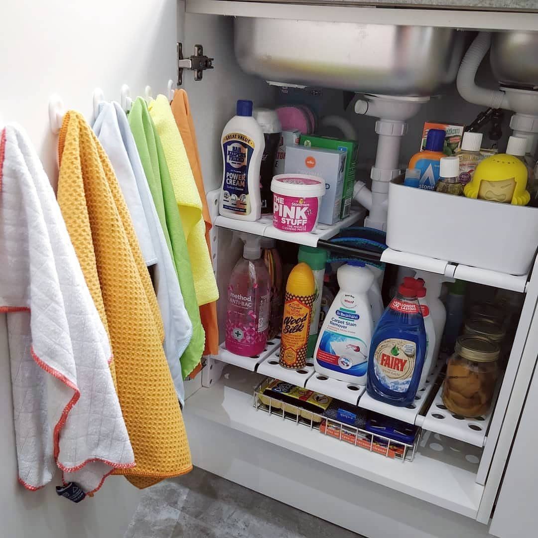 White tiered organizer under a kitchen sink filled with various colorful cleaning supply bottles.