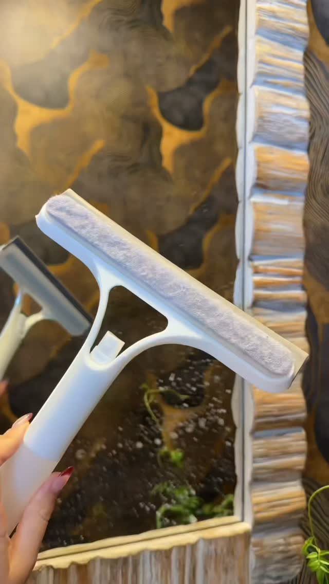 A hand holding a white window squeegee tool against a large decorative mirror.