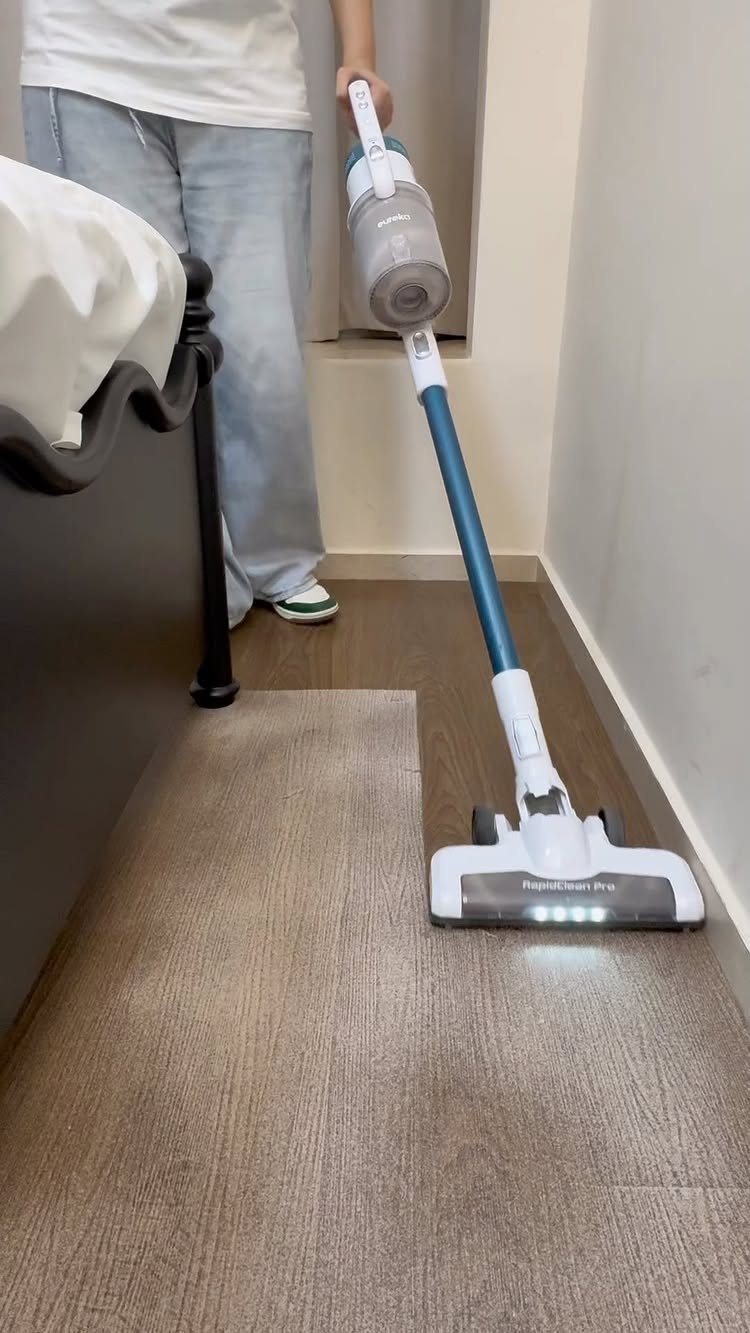 A person vacuuming a light brown rug on a dark wood floor in a room.