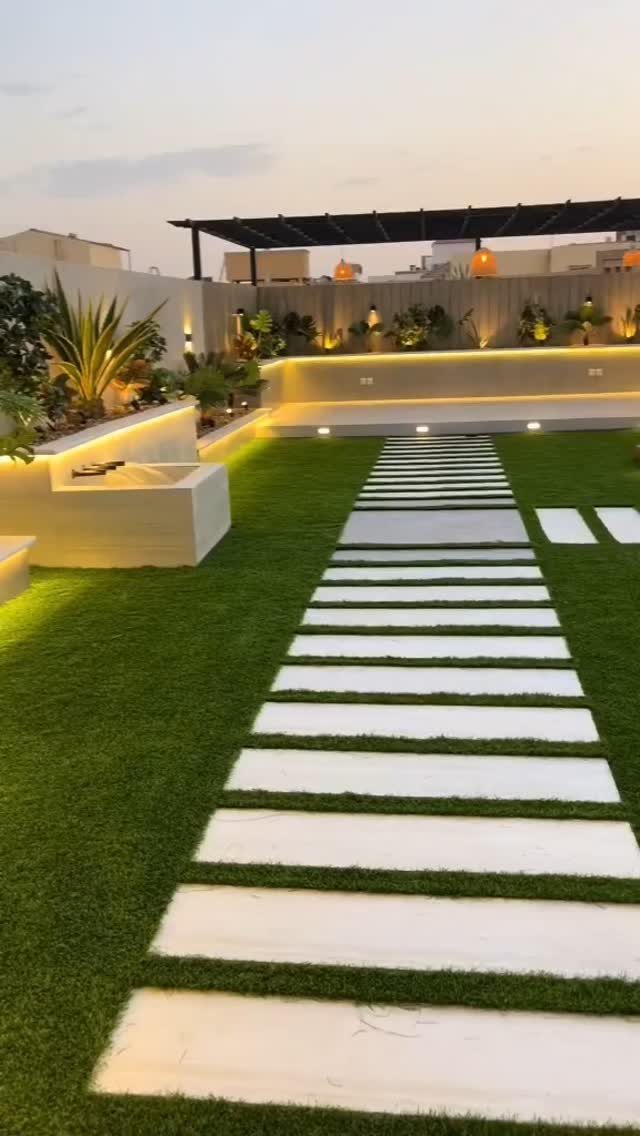White rectangular stepping stones create a path through a manicured green lawn in a modern backyard.