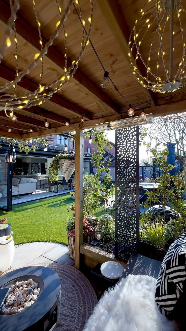 Wooden pergola with hanging string lights overlooking a backyard with a fire pit and lawn.