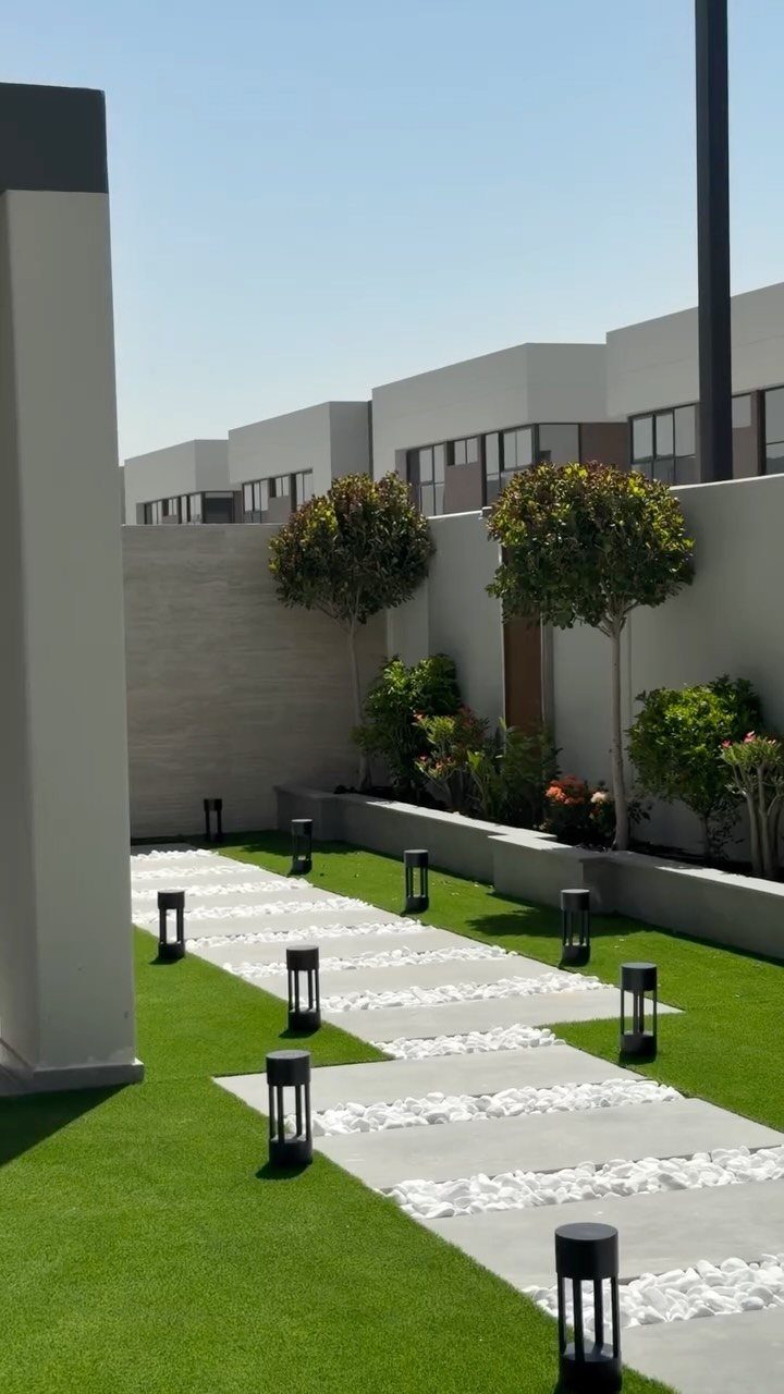 Geometric stone walkway with white pebbles and black lanterns on a green lawn.
