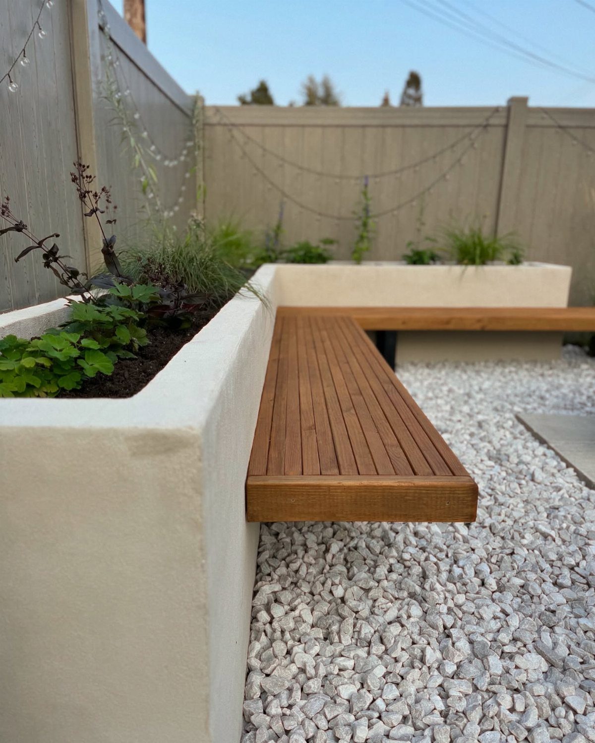 Wooden slat bench integrated into a white concrete raised garden bed surrounded by white gravel.
