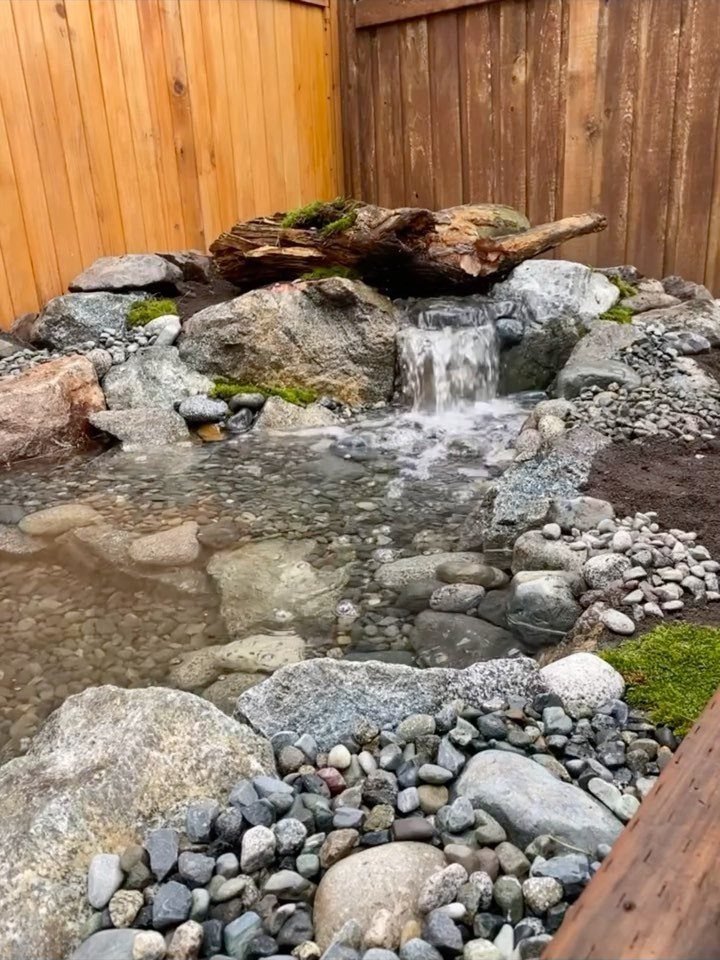 Small backyard water feature with a waterfall flowing over rocks and driftwood.