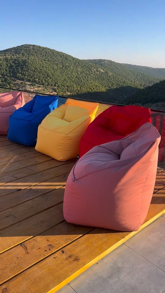 Colorful bean bag chairs arranged on a wooden balcony overlooking green mountains.