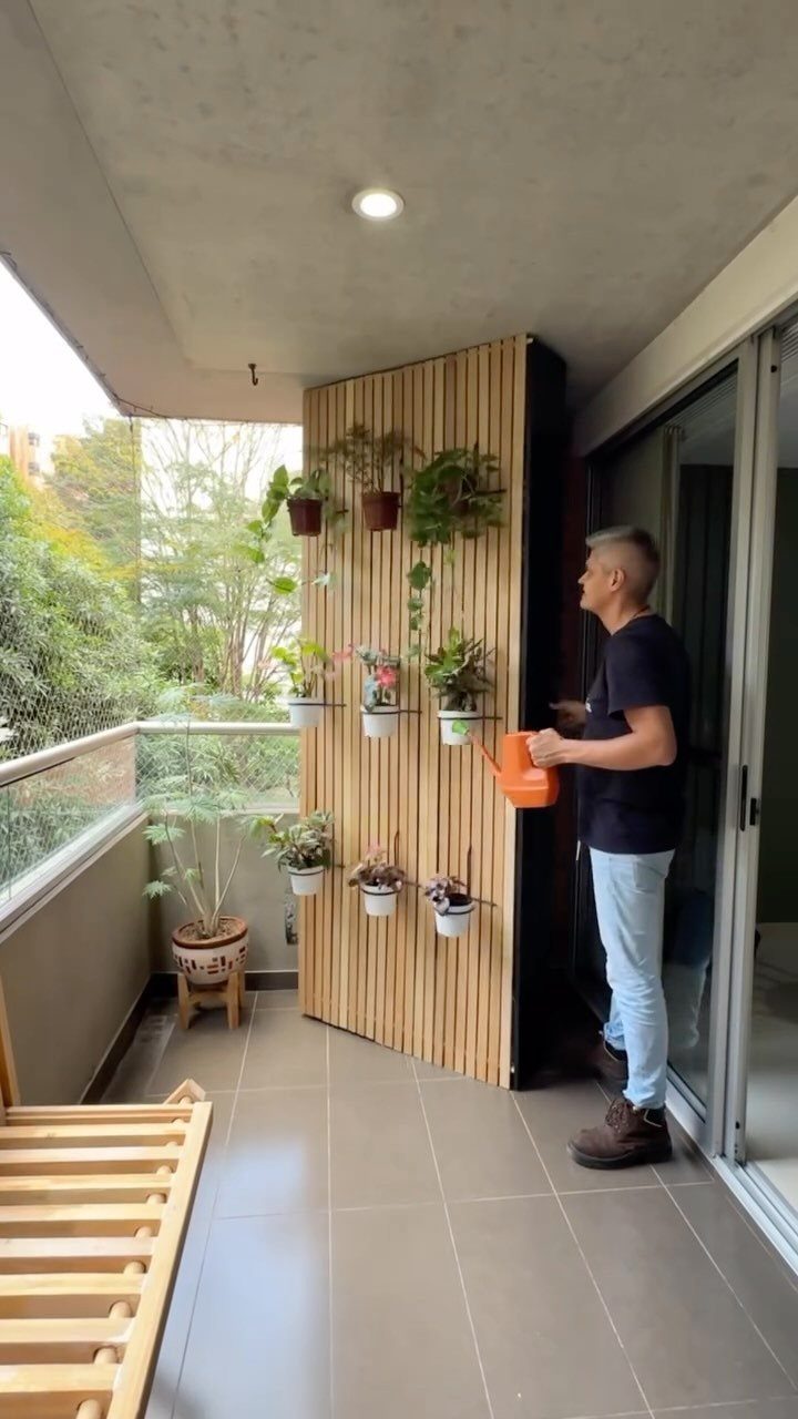 Man watering plants on a balcony with a vertical wooden slat planter wall.