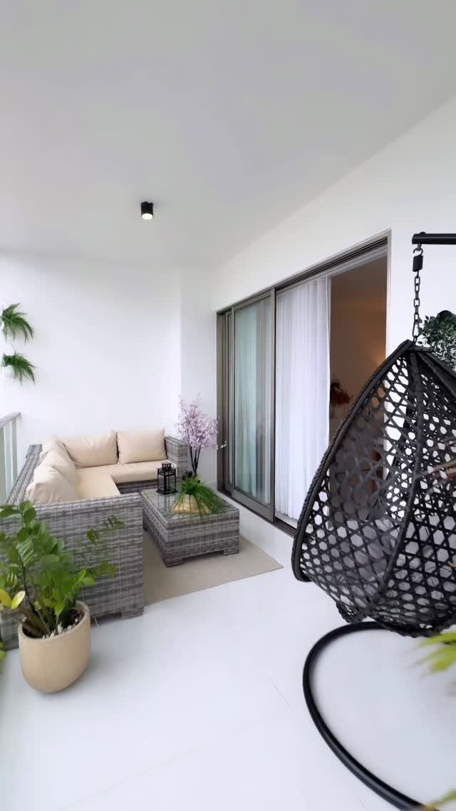Grey wicker sectional sofa with beige cushions and a black hanging egg chair on a white balcony.