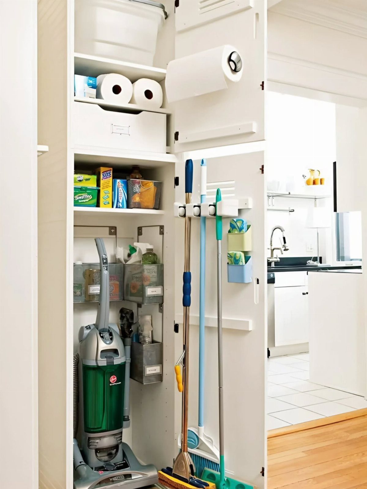 Organized white closet containing a vacuum, cleaning supplies, and hanging mops and brooms.