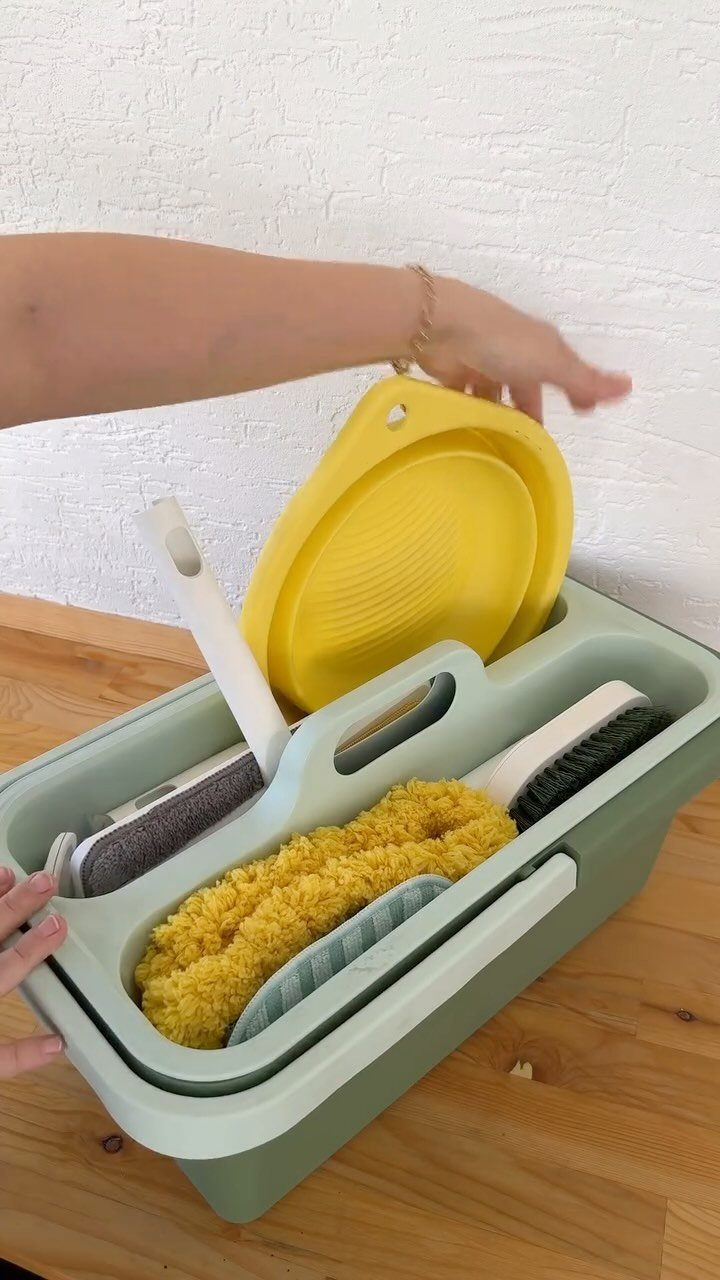 A hand reaches into a green plastic organizer containing various cleaning tools and a yellow lid.