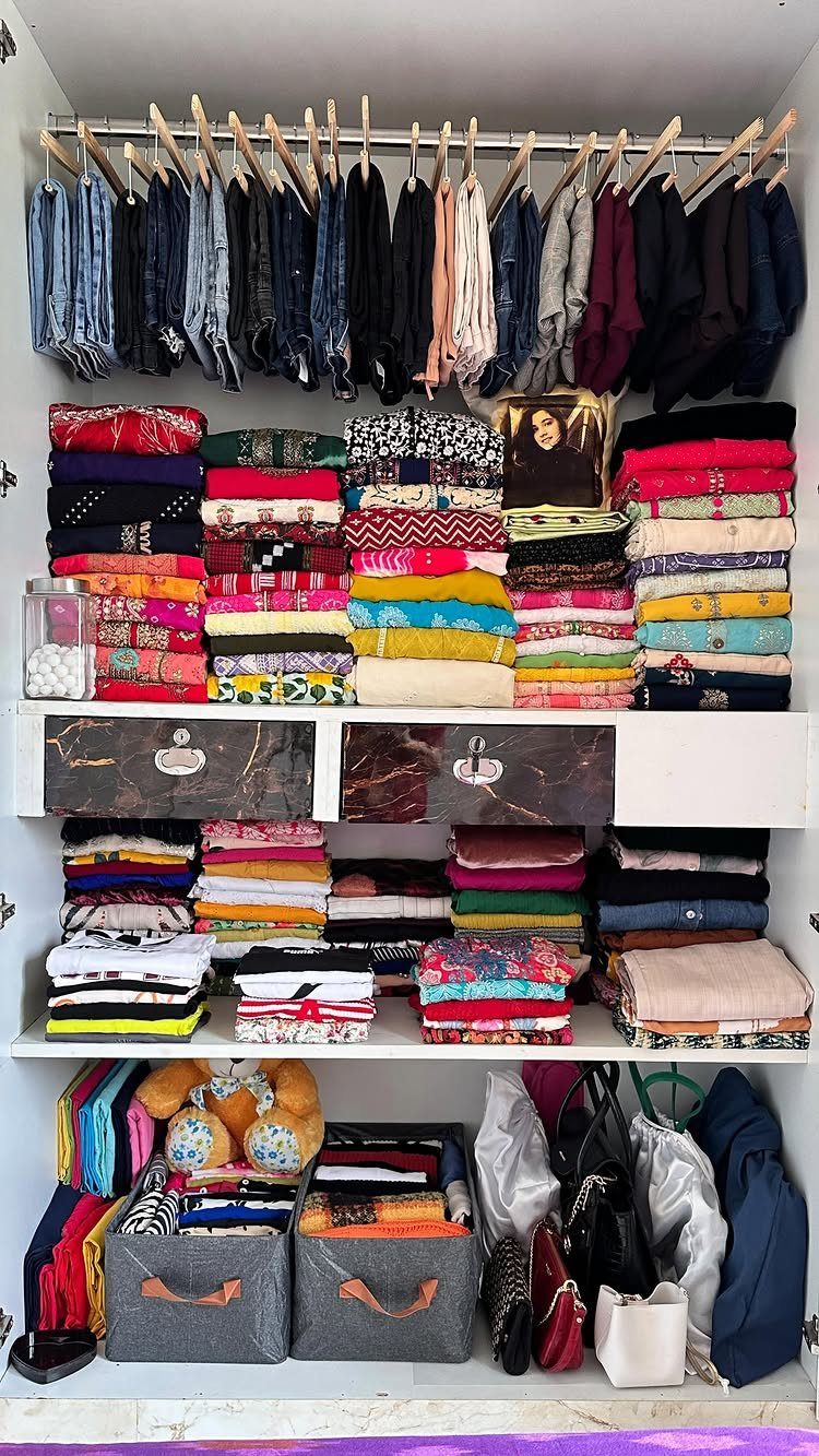 Neatly organized closet with colorful folded clothes, hanging garments, and fabric storage bins.