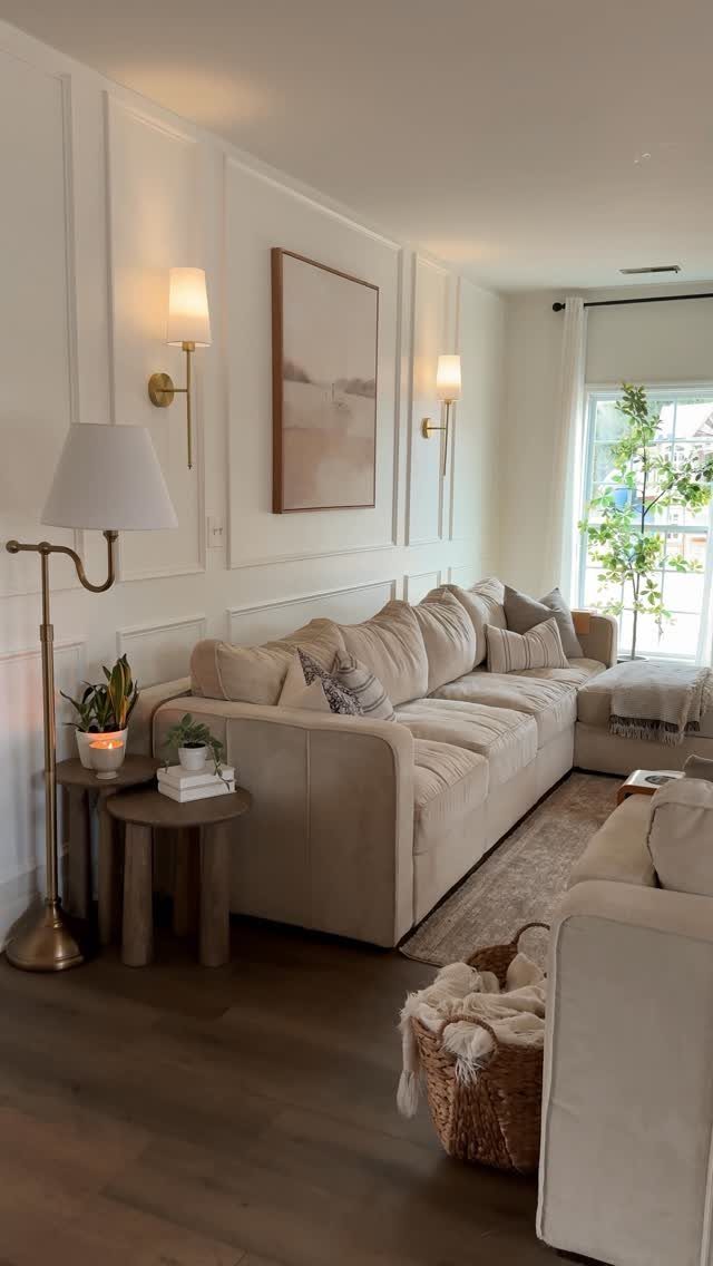 Beige sectional sofa with pillows in a living room with white paneled walls and warm lighting.