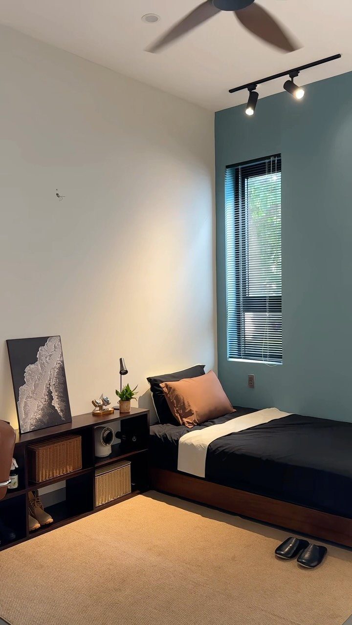 A tidy bedroom with a dark bed, teal accent wall, and organized shelving unit.