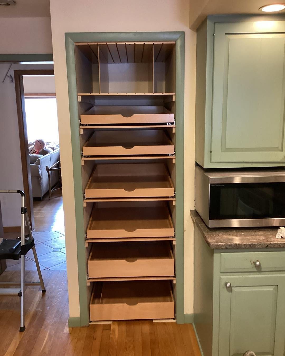 Tall wooden pull-out drawers installed within a narrow, light green pantry shelving unit.