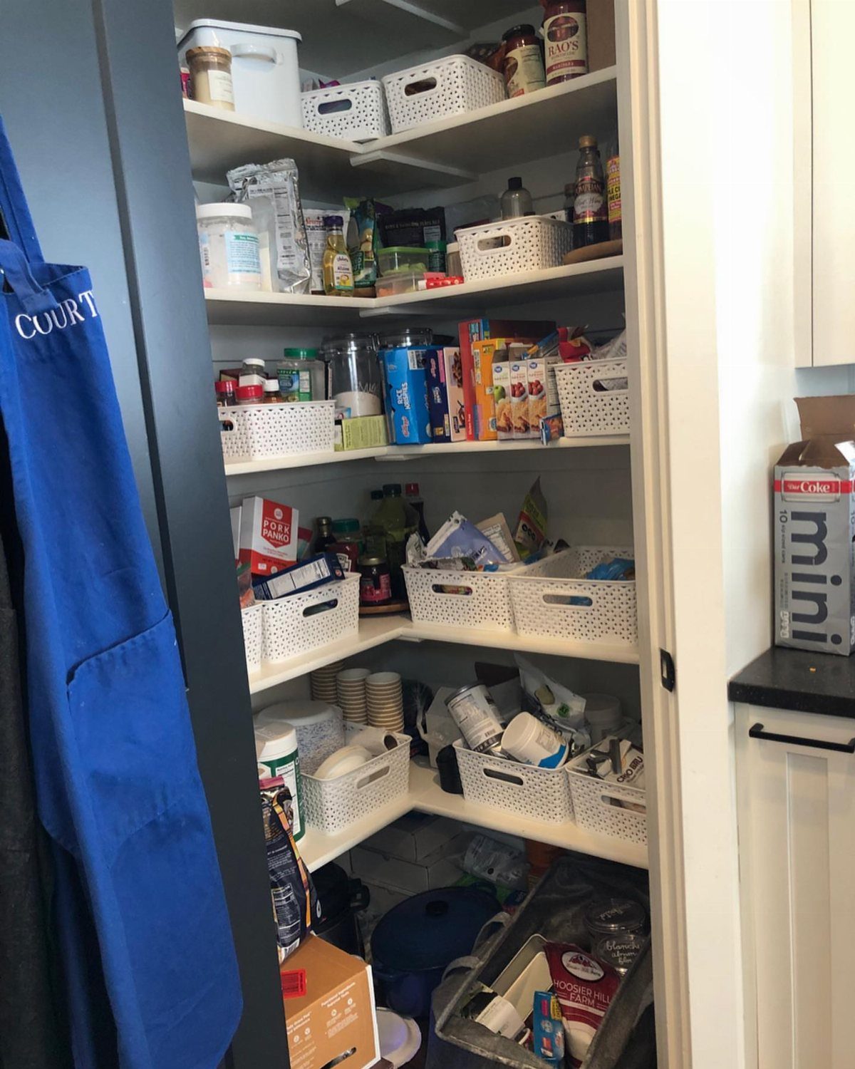 White corner pantry shelves filled with various food items and organized in white baskets.
