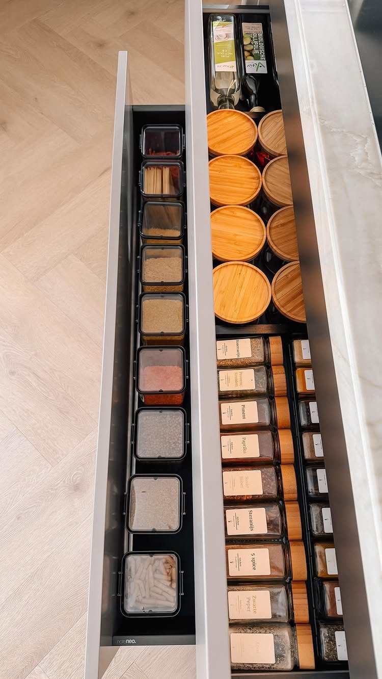 Two narrow kitchen drawers filled with organized spices in glass and wooden containers.