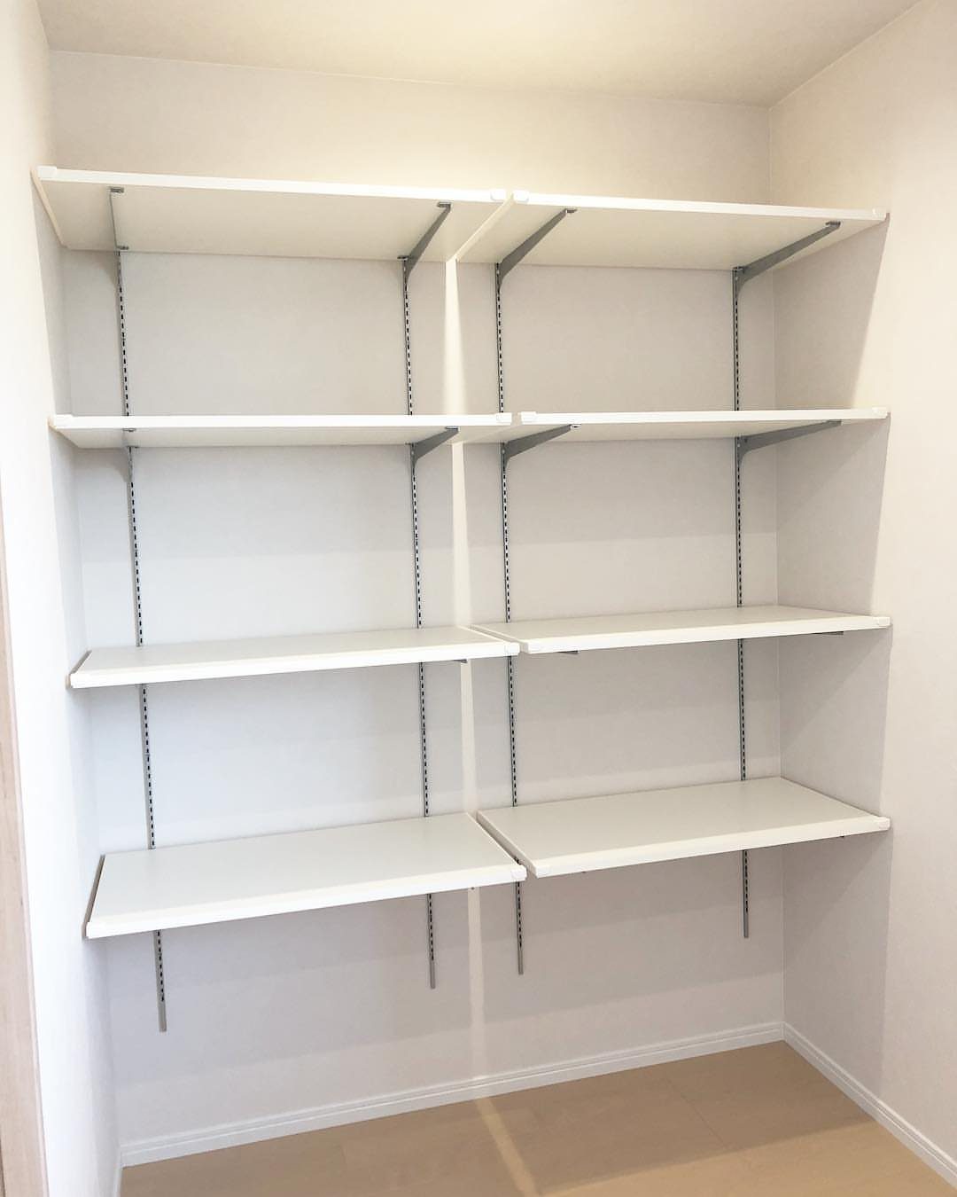 White adjustable shelves mounted on metal tracks inside a clean, white pantry or closet space.
