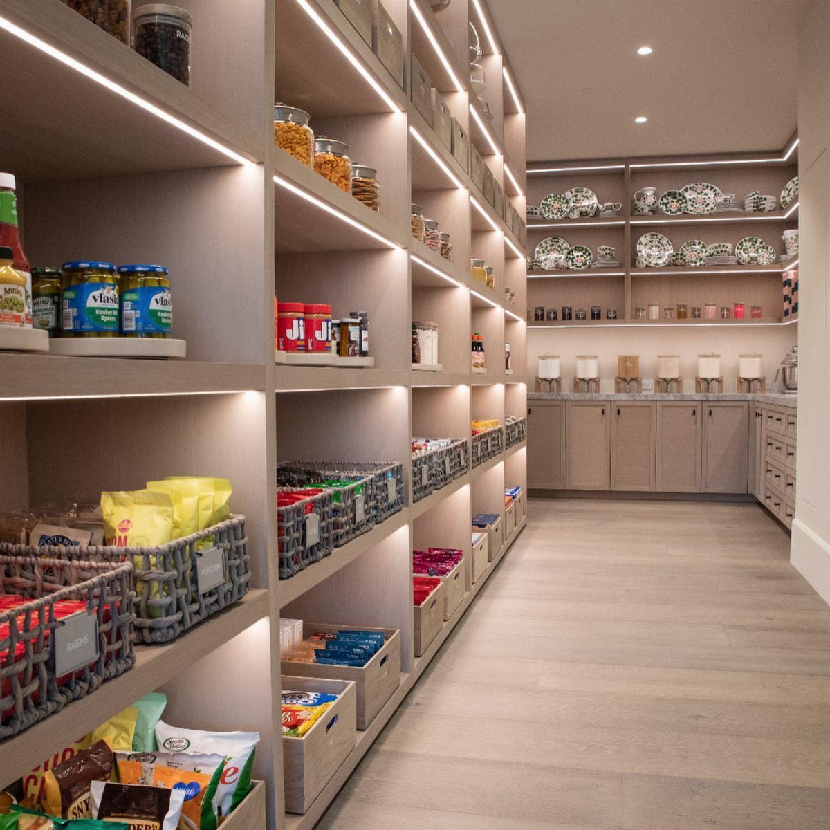 Open pantry shelves with integrated lighting holding organized food items and colorful storage bins.