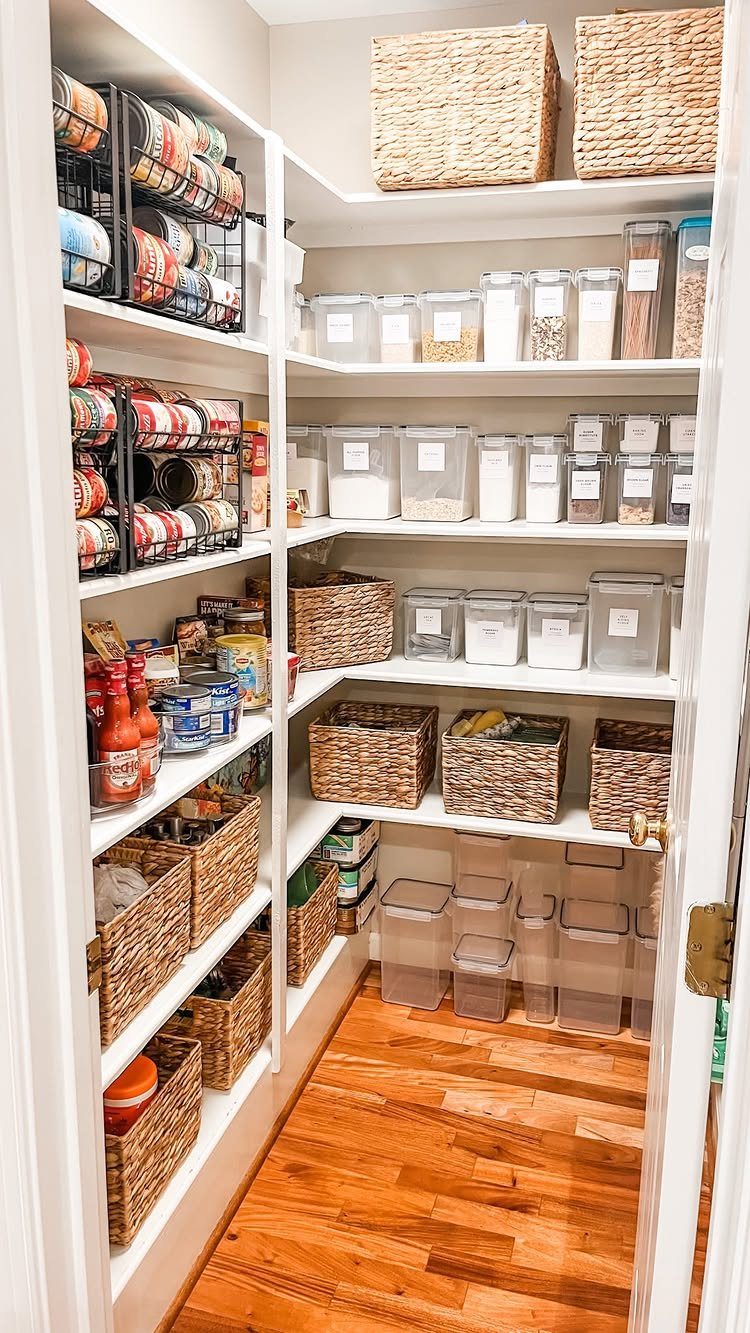 A walk-in pantry featuring white shelves stocked with wicker baskets and clear plastic storage containers.