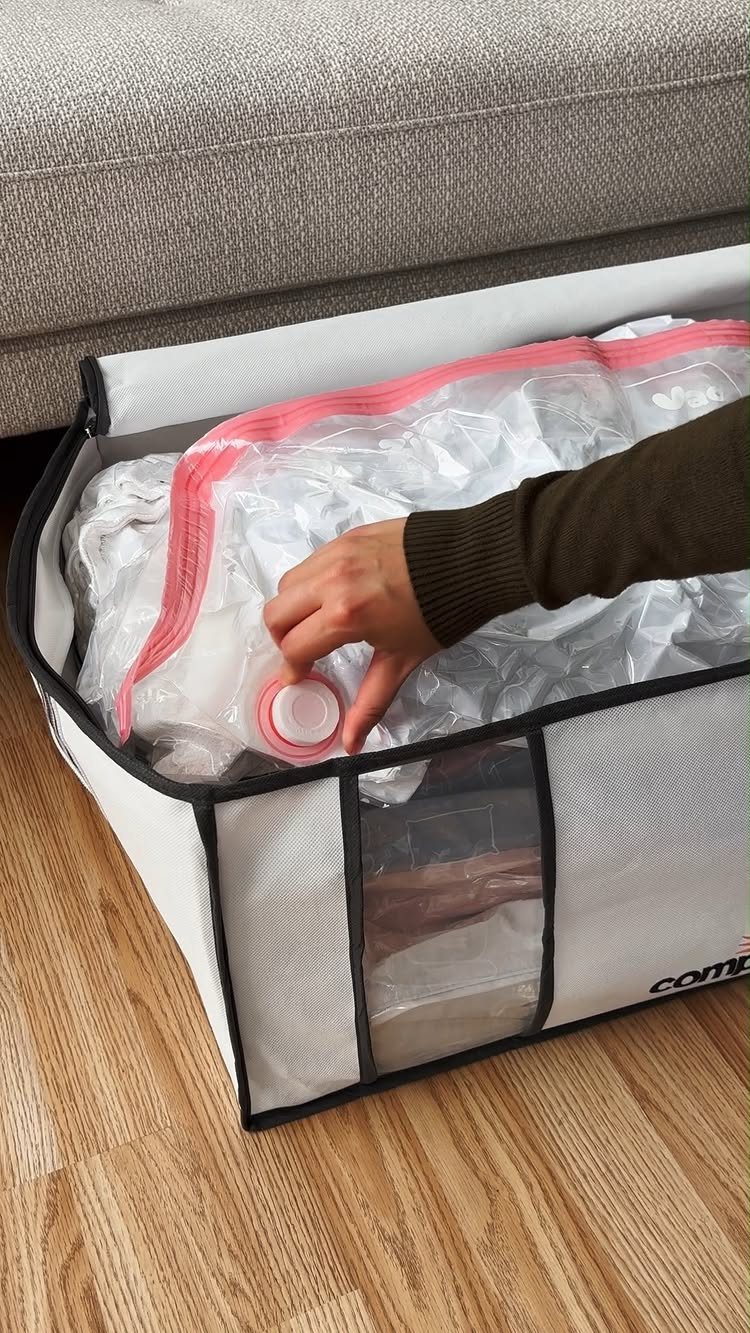Closet Organization: 8 Sweater Storage Ideas That Save Space 2 A hand pressing the valve of a vacuum-sealed bag inside a white storage bin.