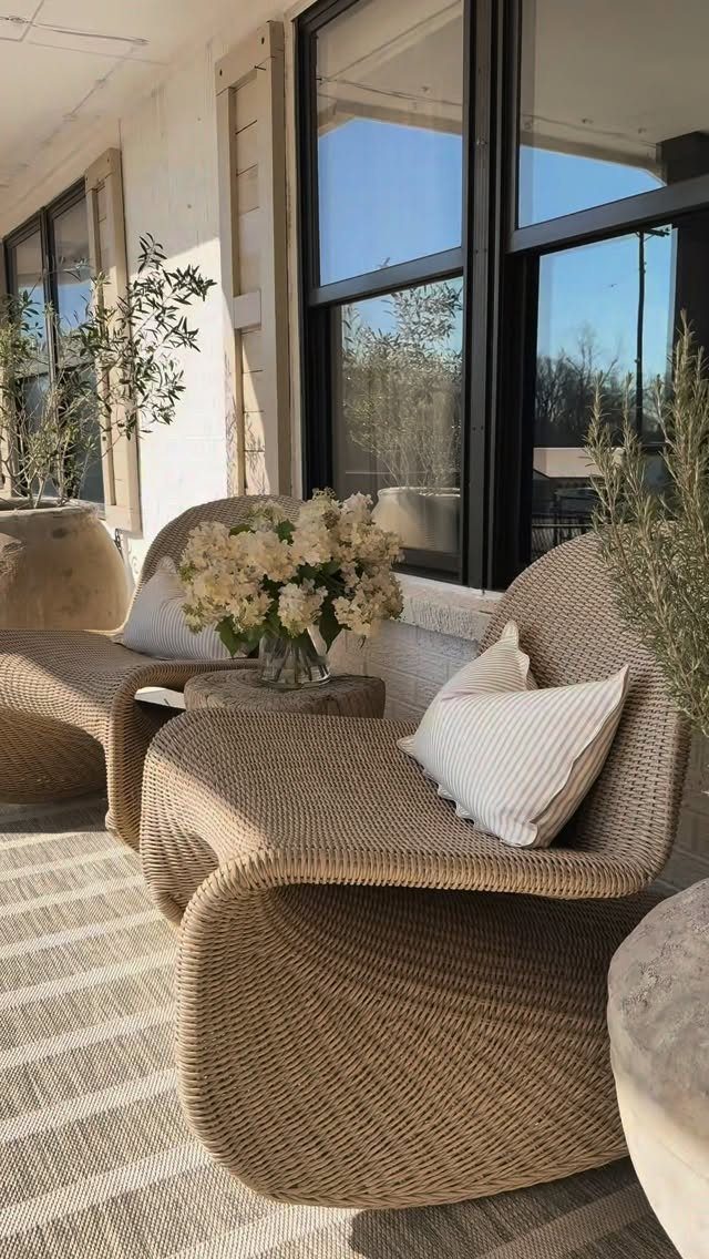 Two sculptural woven wicker lounge chairs with white pillows on a striped rug outdoors.