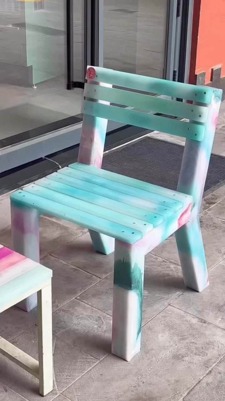 A small chair made from colorful marbled recycled plastic slats on a tiled patio.