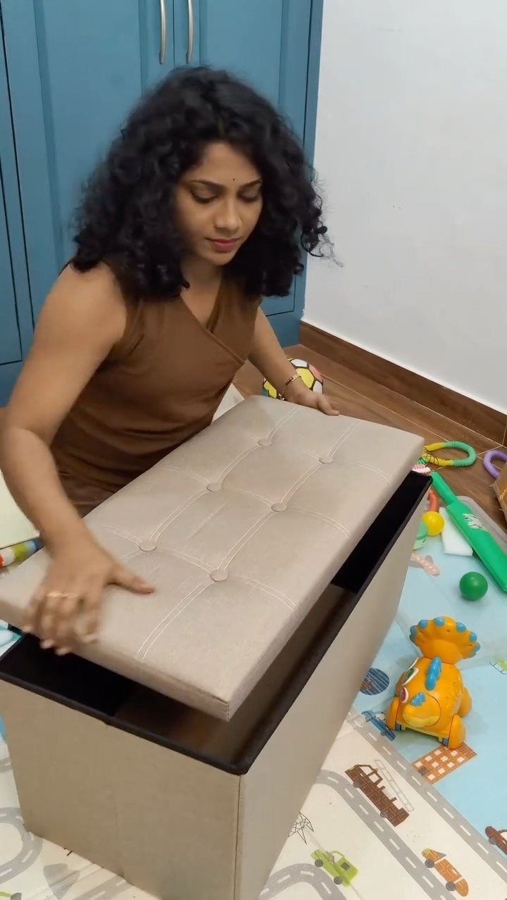 5 Creative Hidden Toy Storage Solutions to Reclaim Your Space 4 A woman lifting the lid of a beige storage ottoman surrounded by colorful children's toys.