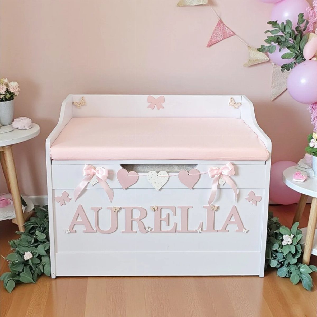 5 Creative Hidden Toy Storage Solutions to Reclaim Your Space 3 White wooden toy chest with pink name lettering and padded lid in a nursery.