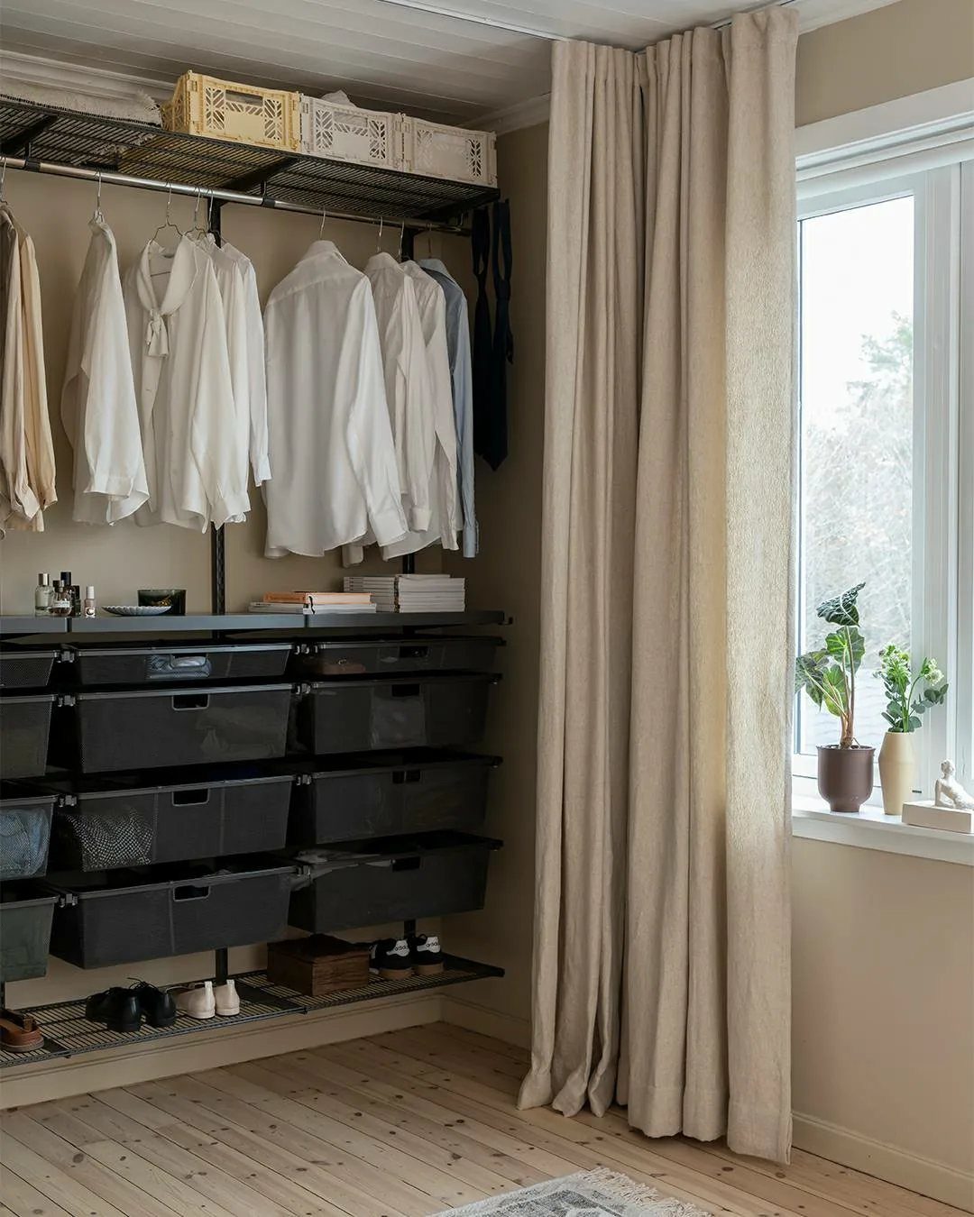 11 Curtain Closet Ideas for Style and Space 5 Beige curtains hanging from a ceiling track next to an open closet with white shirts.
