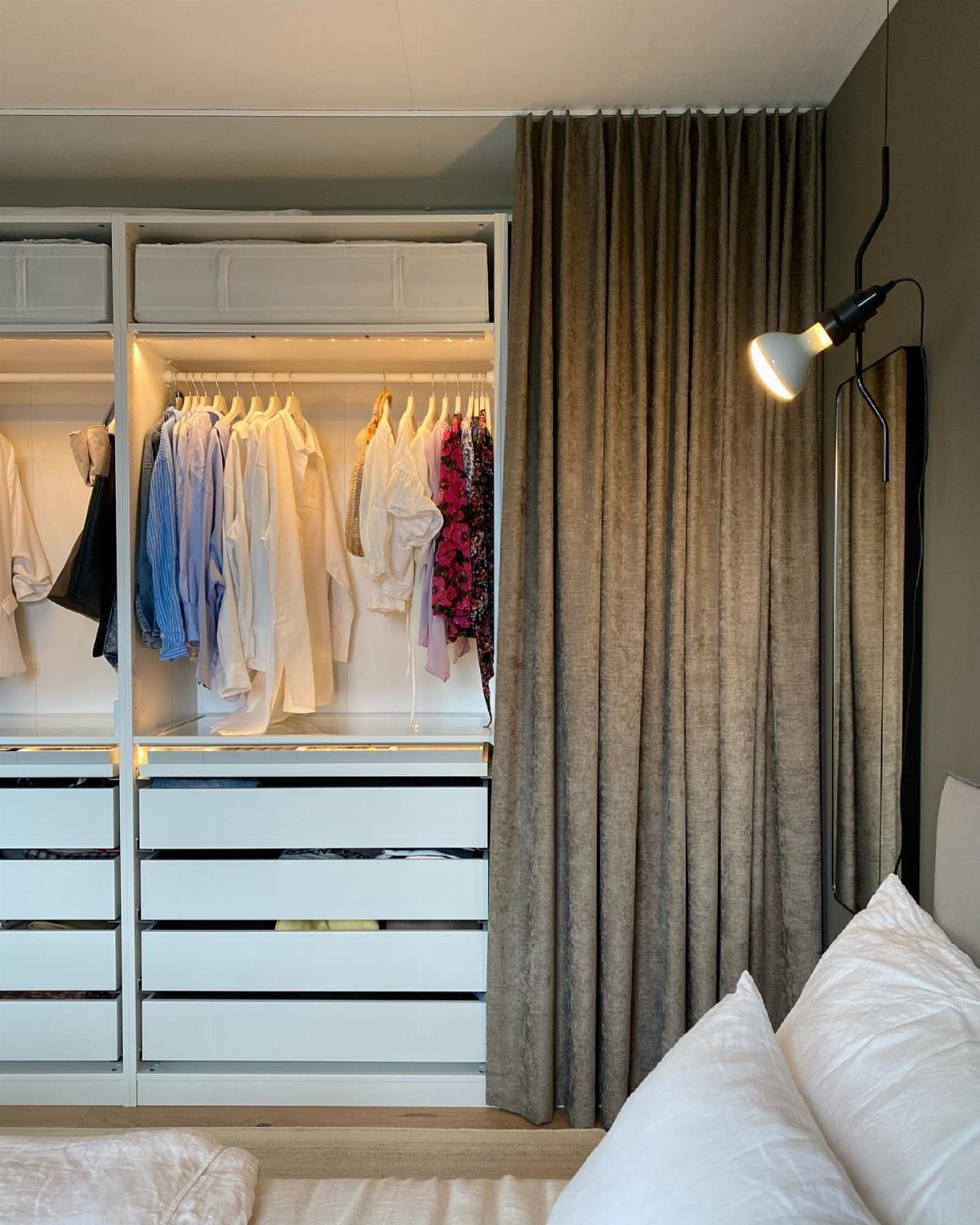 11 Curtain Closet Ideas for Style and Space 1 Neutral beige curtains hanging next to a white built-in wardrobe and a bed with white pillows.