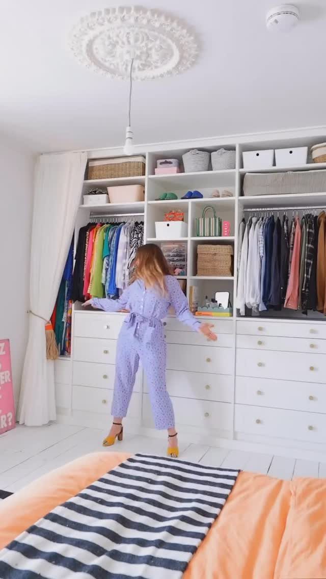 11 Curtain Closet Ideas for Style and Space 10 Woman in purple jumpsuit standing before a large white built-in wardrobe with open shelving and hanging clothes.
