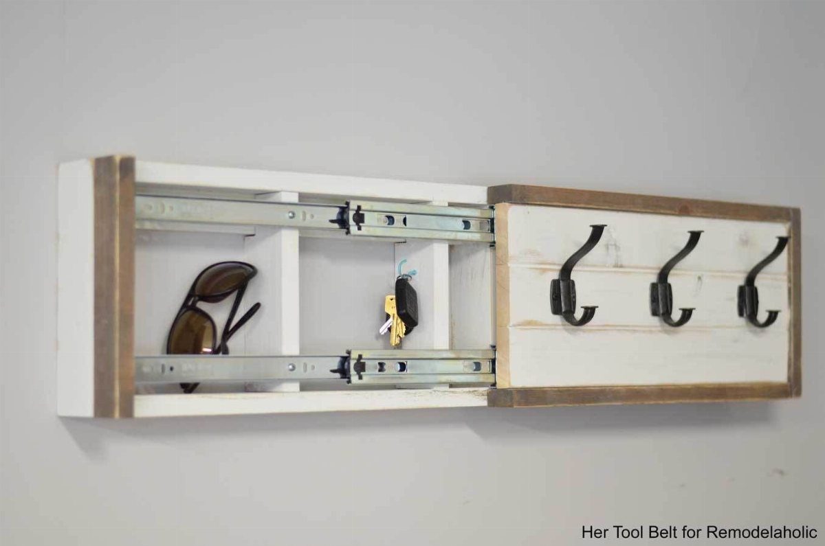 A white wooden coat rack with black hooks sliding open to reveal a hidden storage compartment.