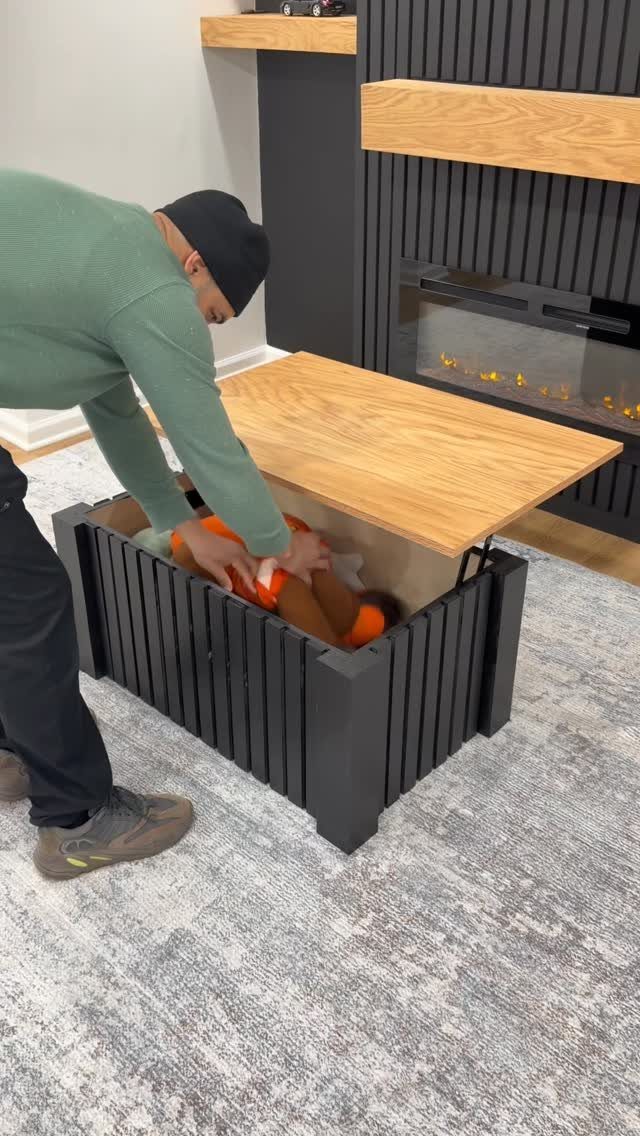 A person placing orange objects into a black slatted coffee table with a wooden top.