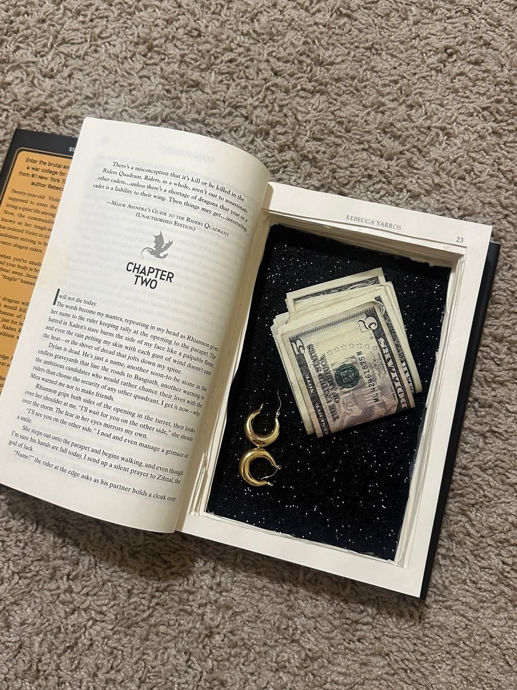 An open book with a hollowed-out center containing cash and a gold earring.