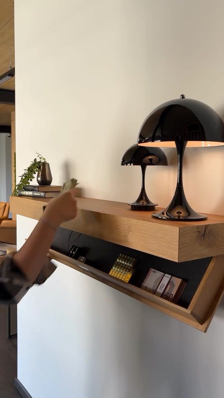 A hand reaches into a secret storage compartment built into a thick wooden floating shelf on a white wall.