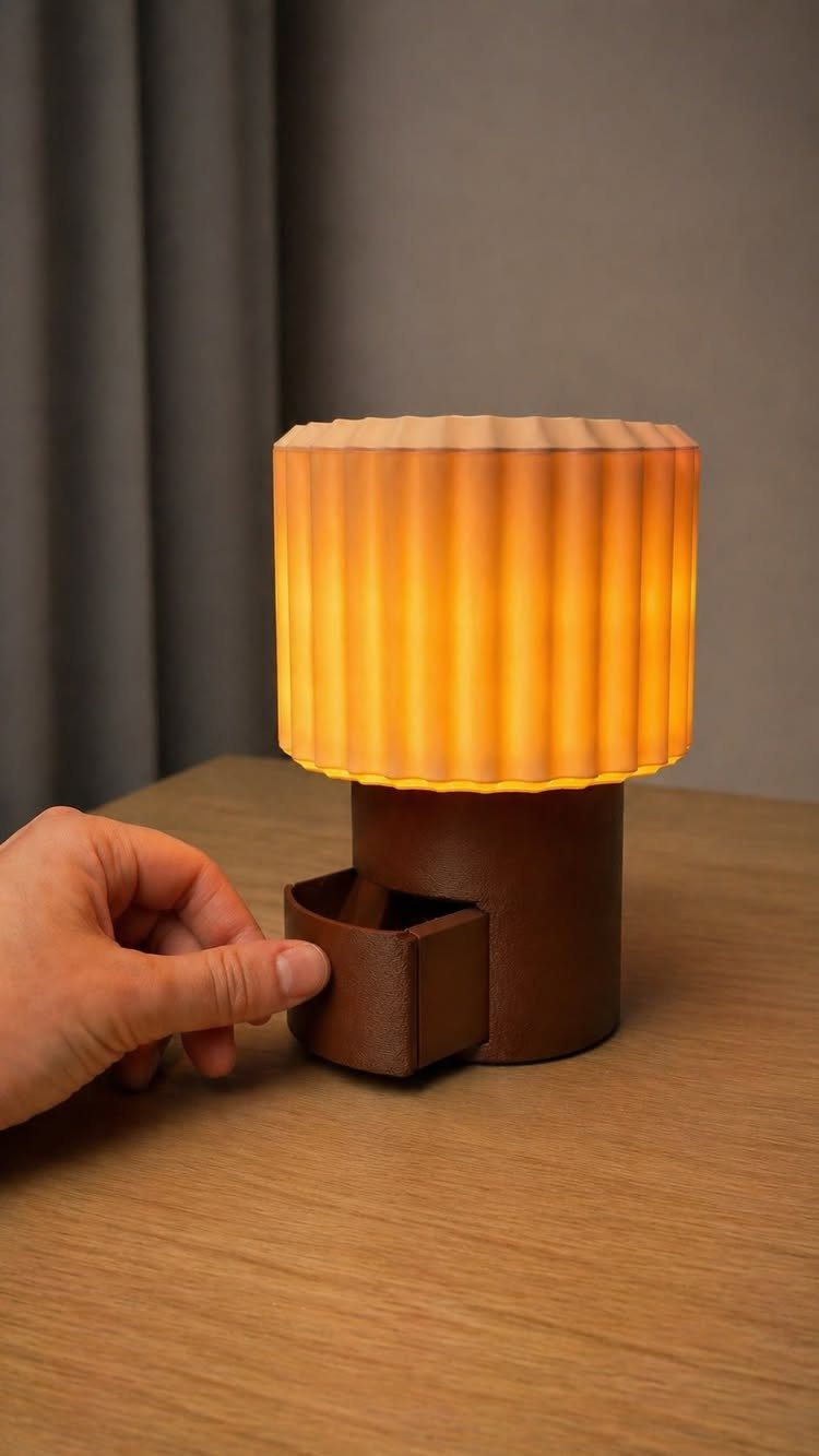 A hand touching a small storage compartment built into the base of a glowing pleated lamp.