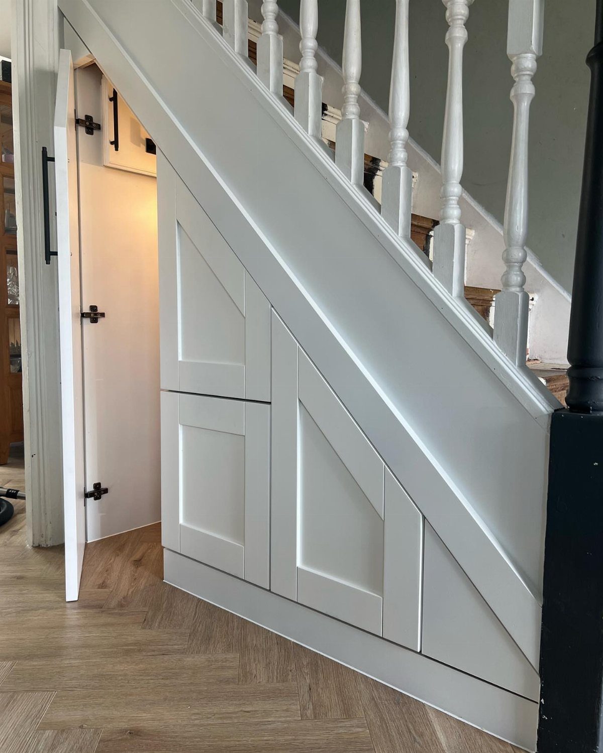 White wooden staircase with built-in storage panels and an open cupboard door showing interior space.