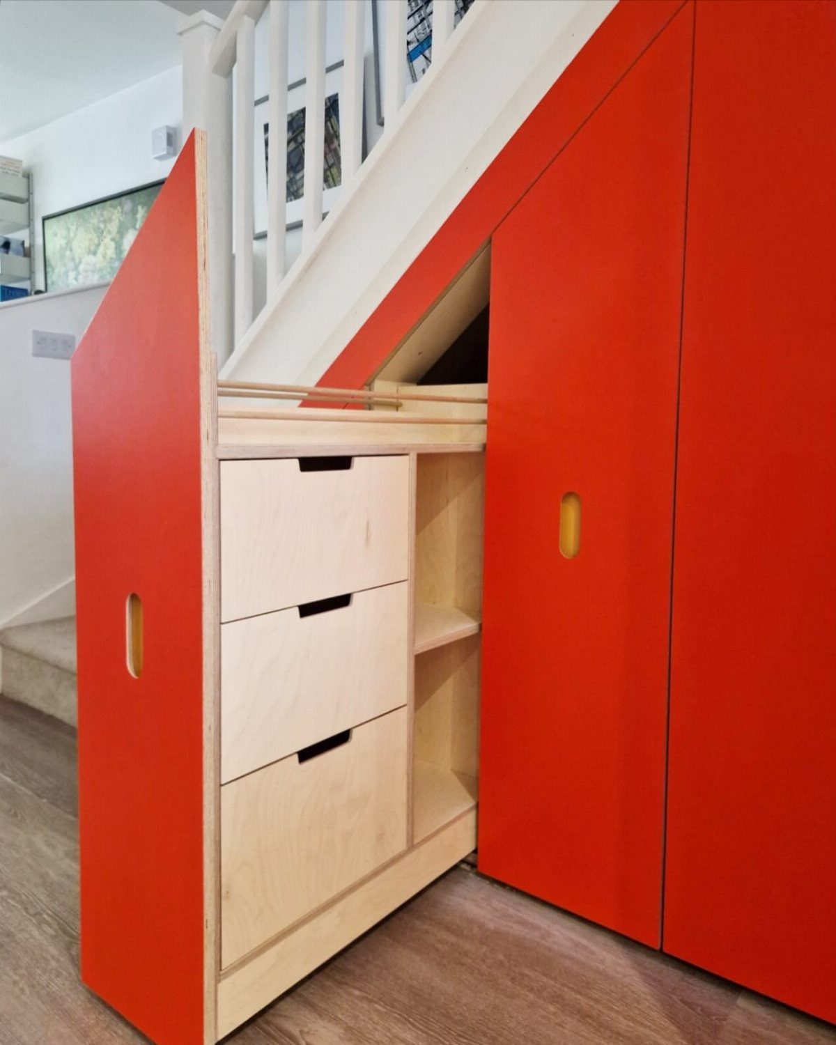 Red and light wood storage drawers built into the space underneath a white staircase.