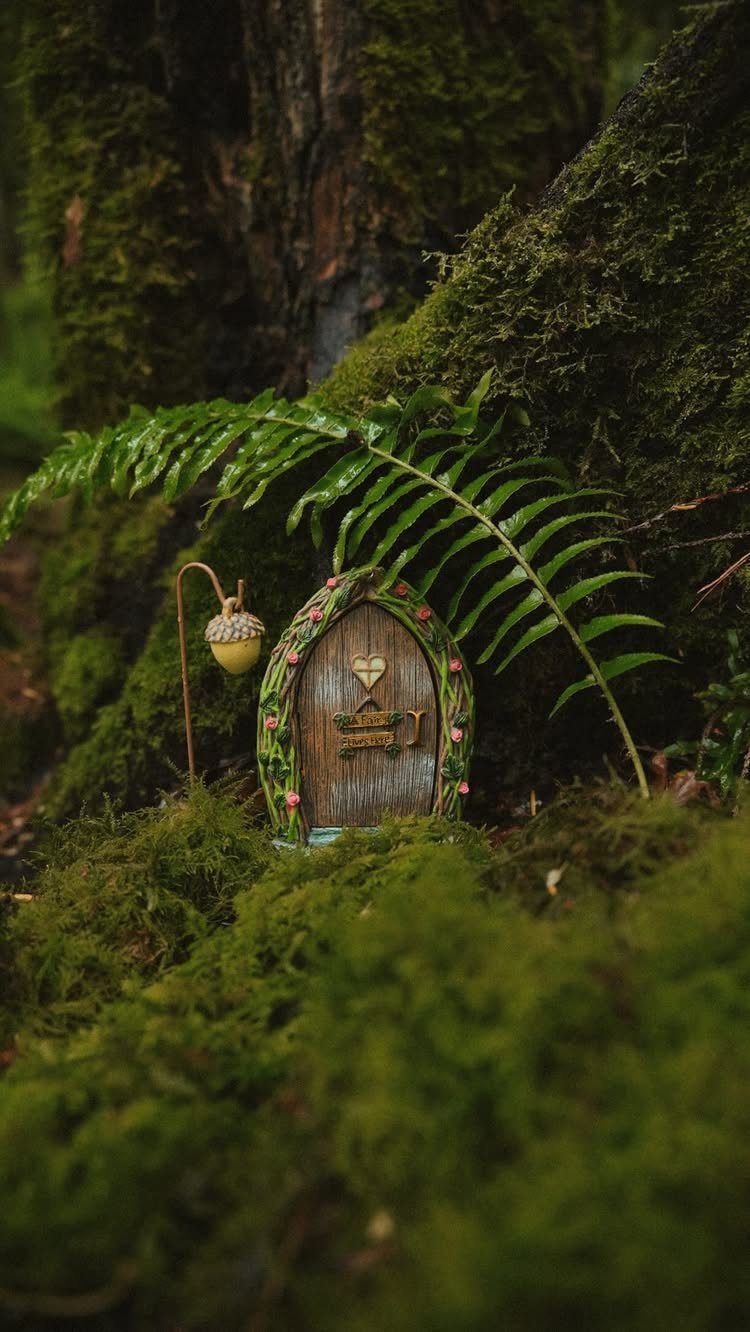 23 Fairy Garden Ideas for Tiny Houses, Teacups and Tree Trunks 8 A miniature wooden fairy door decorated with moss and flowers at the base of a mossy tree.