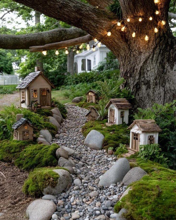 23 Fairy Garden Ideas for Tiny Houses, Teacups and Tree Trunks 7 Small wooden fairy houses arranged around a pebble path and mossy landscape under a tree.