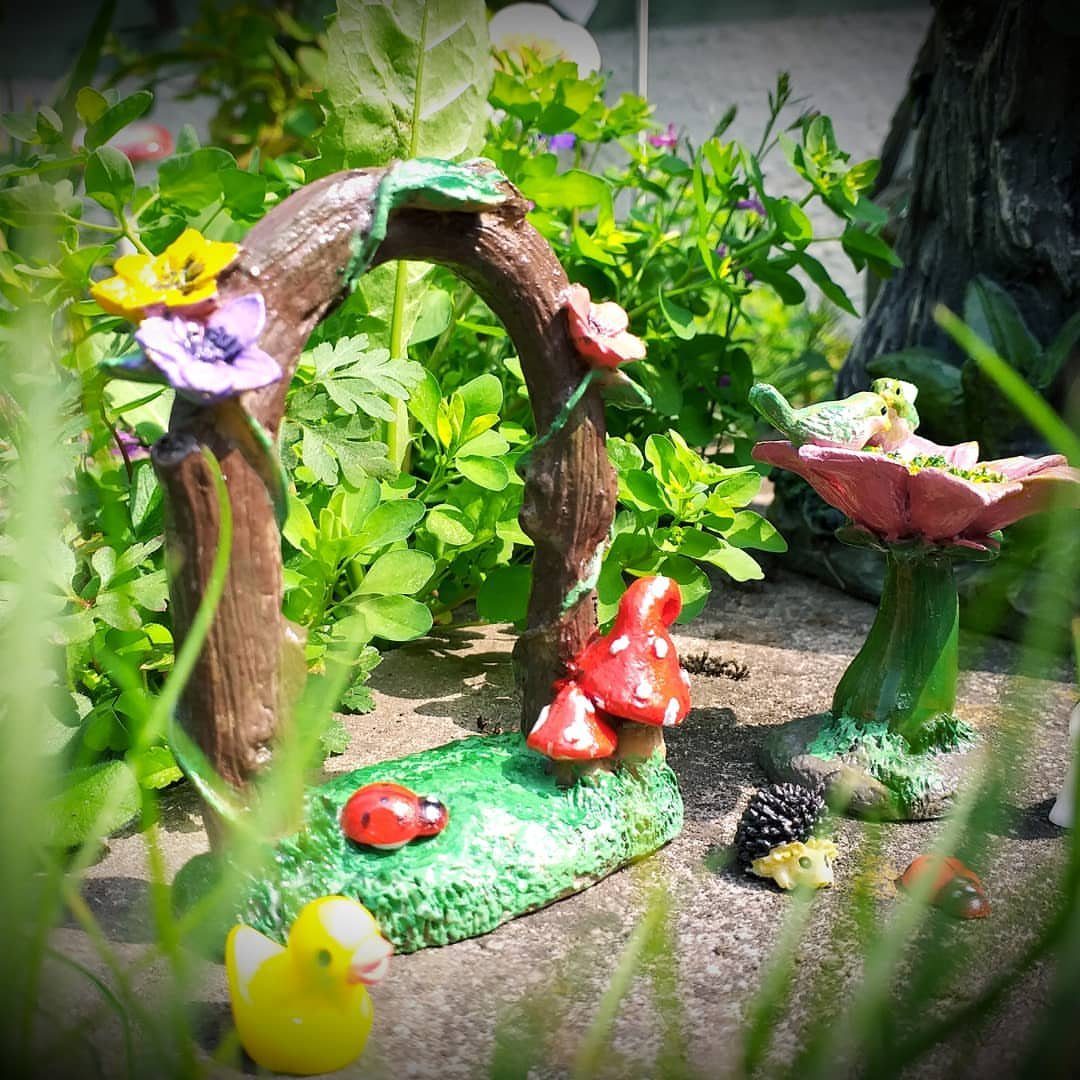 23 Fairy Garden Ideas for Tiny Houses, Teacups and Tree Trunks 10 A miniature tree-bark flower arch decorated with colorful blossoms in a lush green garden.