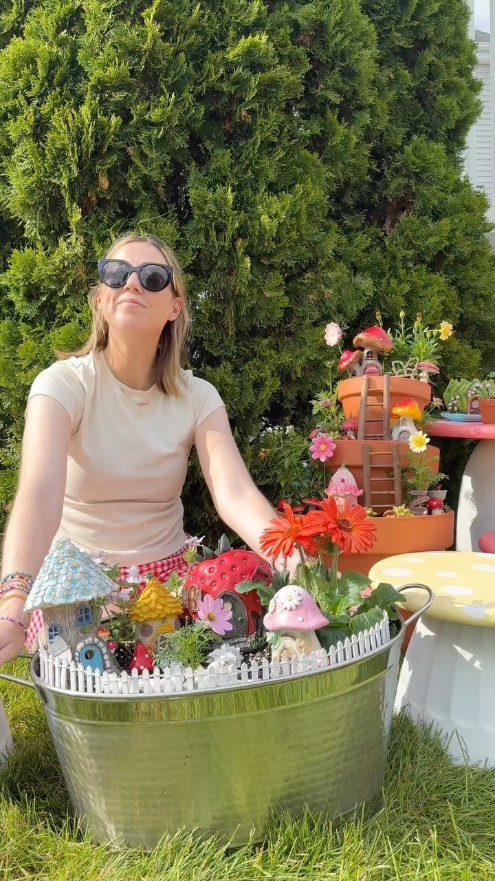 23 Fairy Garden Ideas for Tiny Houses, Teacups and Tree Trunks 16 A woman sitting in a garden next to a metal tub containing a miniature fairy garden.