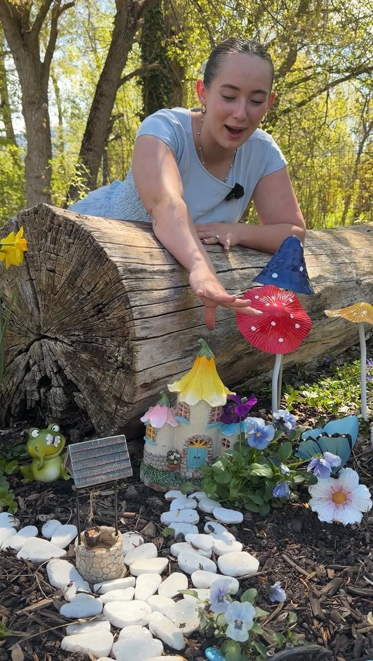 23 Fairy Garden Ideas for Tiny Houses, Teacups and Tree Trunks 23 A woman points toward a miniature fairy garden featuring a small house and mushrooms near a log.