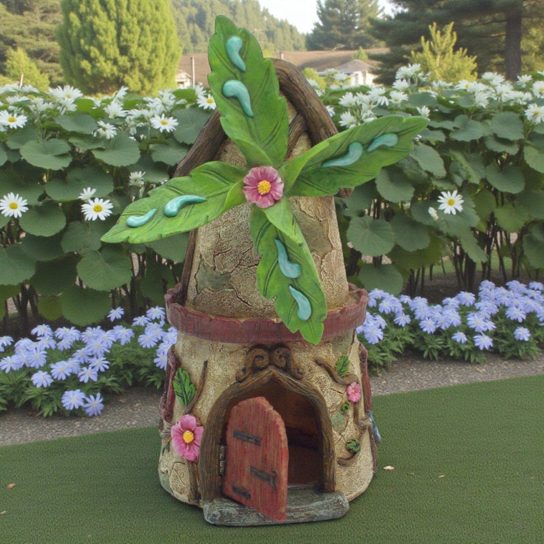 23 Fairy Garden Ideas for Tiny Houses, Teacups and Tree Trunks 13 A miniature stone windmill with green leaf blades and pink flower decorations on green grass.