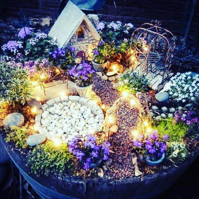 23 Fairy Garden Ideas for Tiny Houses, Teacups and Tree Trunks 21 A miniature fairy garden with a small stone house and glowing lights inside a wooden barrel.