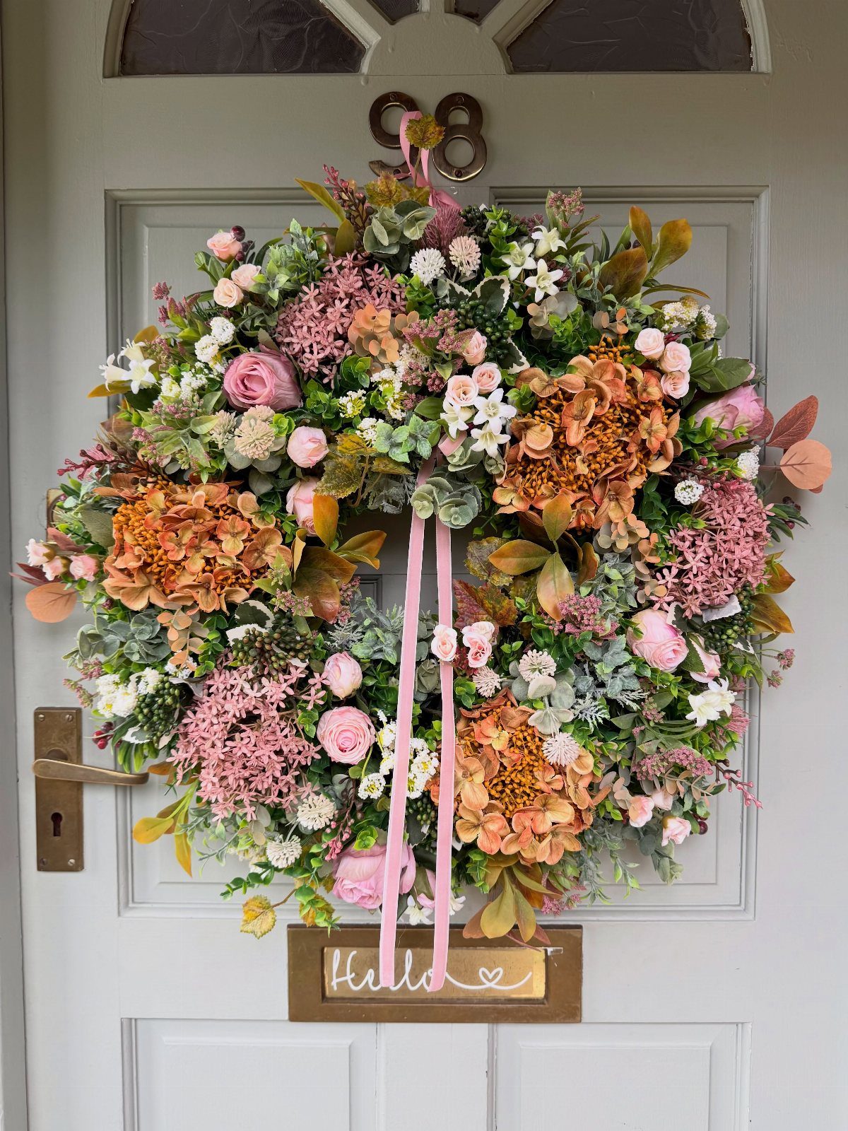 14 Front Porch Decorating Ideas for Every Season 7 A large floral wreath with pink roses and orange hydrangeas hanging on a grey front door.