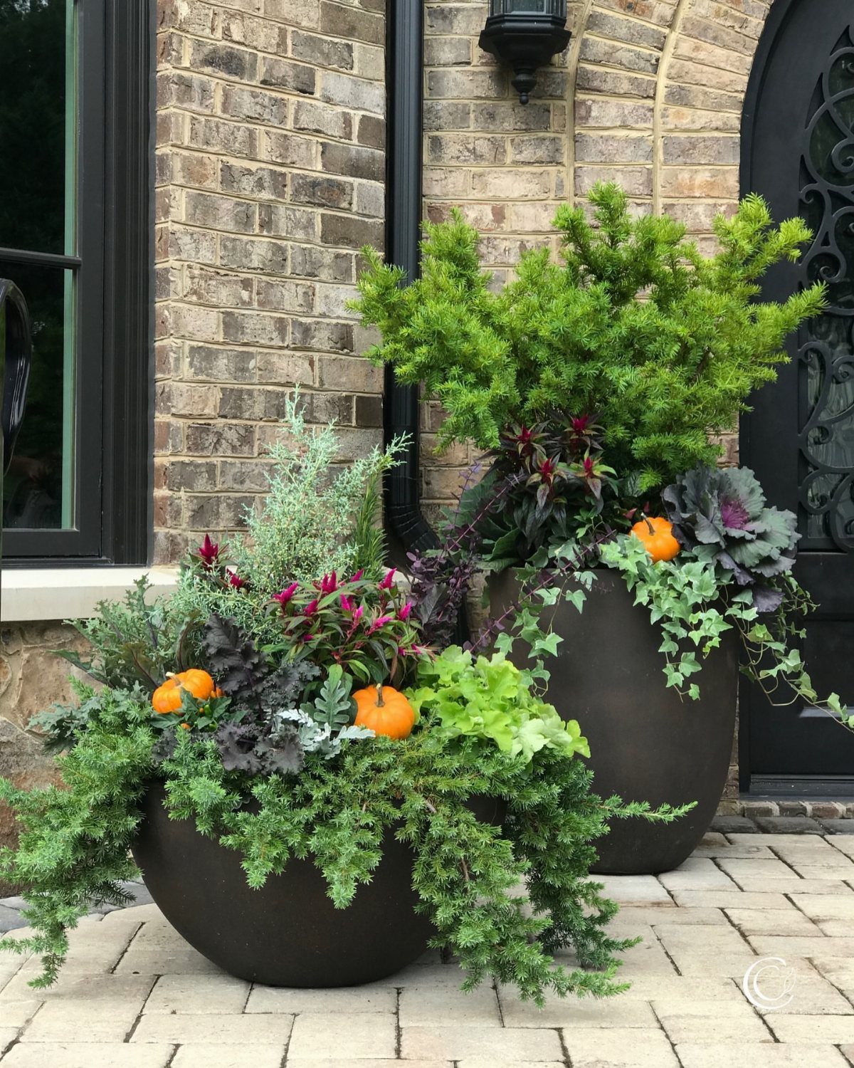 14 Front Porch Decorating Ideas for Every Season 1 Two large dark planters filled with lush green plants and ornamental cabbage on a stone porch.
