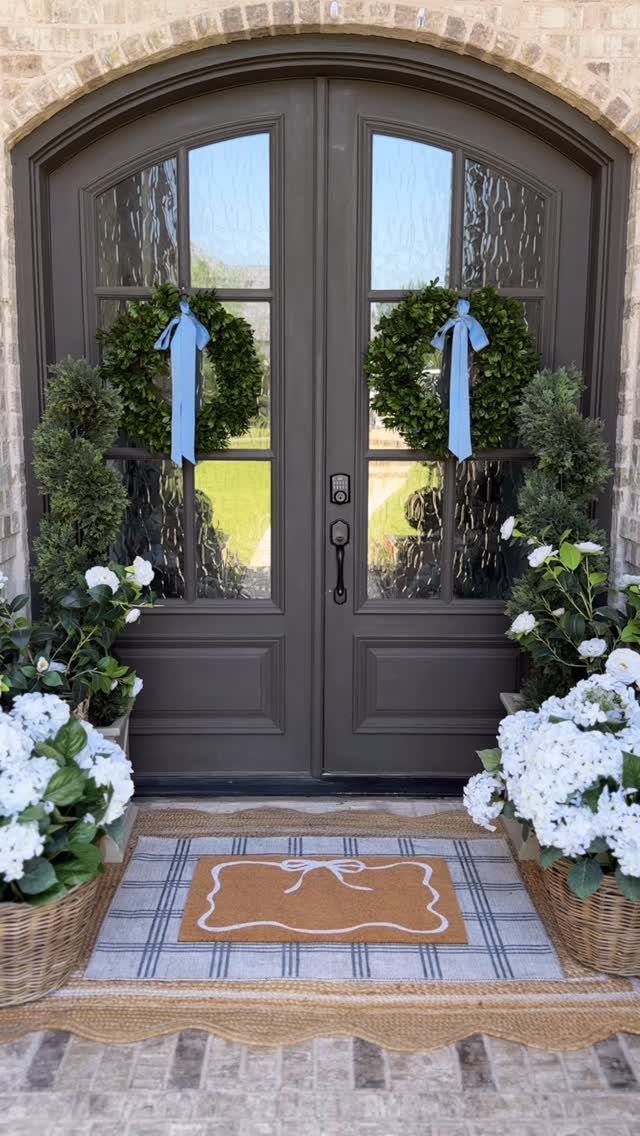 14 Front Porch Decorating Ideas for Every Season 3 A decorative bow doormat layered over a blue plaid rug in front of dark double doors.