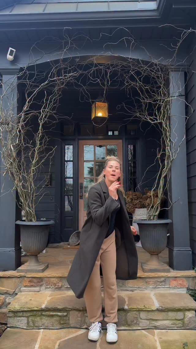 14 Front Porch Decorating Ideas for Every Season 9 A woman posing on stone steps between two large matching planters with tall branches.